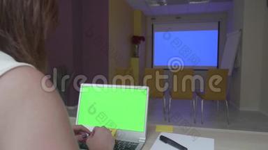 女士坐在桌旁，手提电脑，绿色<strong>屏</strong>幕在蓝色投影仪<strong>屏</strong>幕前，类型和滚动<strong>屏</strong>幕，而